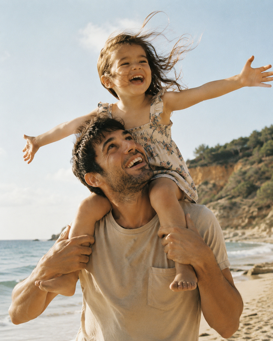 A father carrying his laughing daughter on his shoulders at the beach